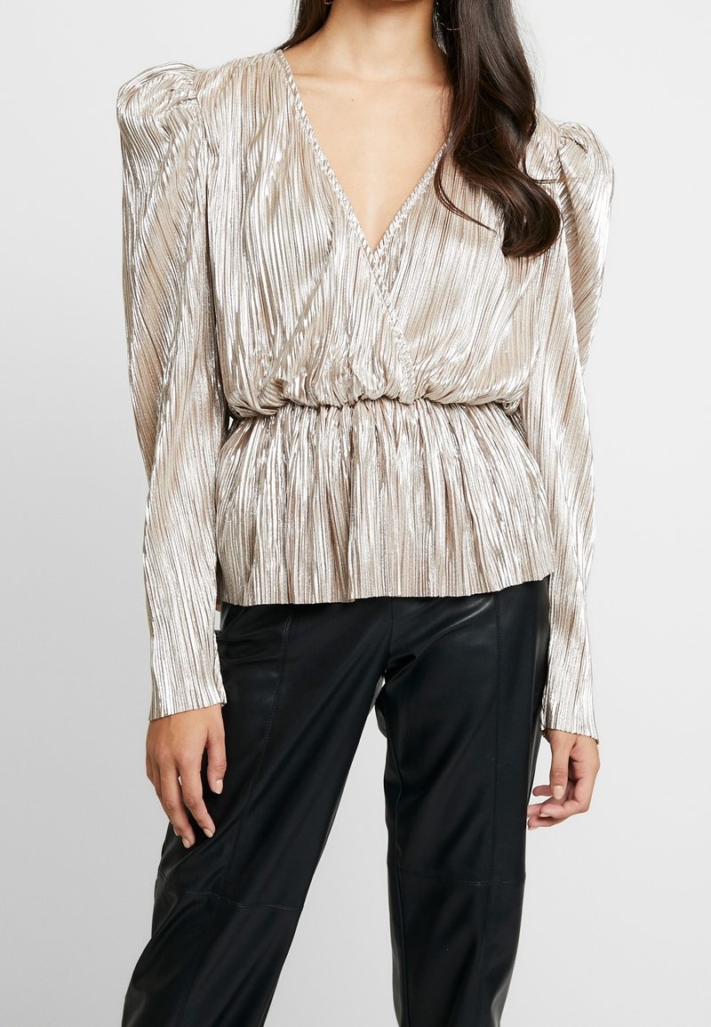 Shiny, pleated metallic top featuring a deep V-neck and puffed sleeves, cinched at the waist, paired with black leather pants.