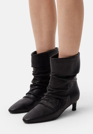 Stivaletti neri in pelle con un design morbido, punta affusolata e dettagli con risvolto. Presentano un modestissimo tacco kitten per un'altezza extra.