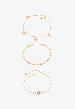 Trzy złote bransoletki na łańcuszku: górna z zawieszkami w kształcie kwiatów i ptaków, środkowa to gruby łańcuch typu curb, dolna z delikatnymi zawieszkami w formie klucza i kamienia szlachetnego.