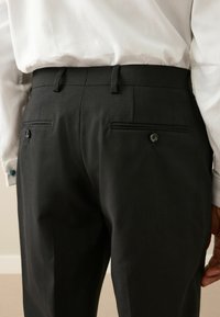 Fekete, testre szabott nadrág sima felülettel, két hátsó zsebbel és gombos záródással, fehér inggel párosítva.