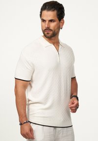 Kurzarm-Polohemd in Off-White, strukturiertem Strick, mit Reißverschluss am Kragen, schwarzen Bündchenakzenten und einer lockeren Passform.