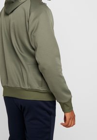 Felpa verde oliva con un design semplice, dotata di tasca a marsupio e polsini a costine. Texture liscia e vestibilità comoda.