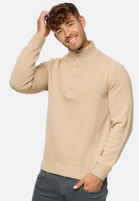 Pull en tricot beige avec un col montant et un boutonnière à quatre boutons. Caractéristiques : poignets et ourlet côtelés. Texture lisse, design léger.
