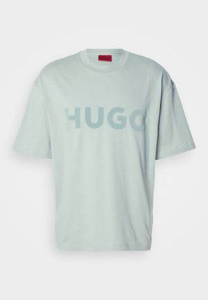 Gaišais piparmētru zaļais pārāk liels īsām piedurknēm T-krekls ar izceltu "HUGO" tekstu uz krūtīm un sarkanu etiķeti apkakles iekšpusē.