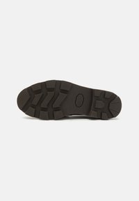 Semelle de chaussure en caoutchouc noir avec une surface texturée et des motifs de crampons marqués pour une meilleure adhérence. Présente un détail de logo en relief au centre.