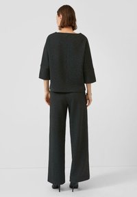 Zwart gestructureerd tweedelig outfit met een brede, rechte broek en een kort mouwen top met een bootneklijn, afgemaakt met hoge hakken.