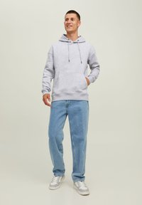 Gray cotton hoodie with a front pocket, drawstring hood, and ribbed cuffs, paired with light blue jeans and gray sneakers.