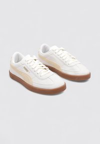 Zapatillas blancas con parte superior de cuero texturizado y acentos de ante en tono marrón claro, con suela de goma y diseño de cordones, que exhiben una marca minimalista.