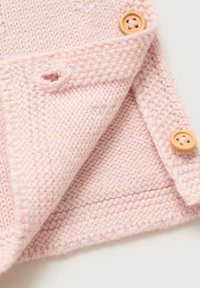 Pletená deka v jemné růžové barvě, s texturovaným vzorem, s okrajem a dvěma dřevěnými knoflíky pro zapínání.