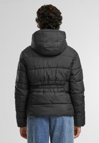 Svart boblejakke med hette, har innsnørt midje, quiltet design og lange ermer. Glatt tekstur, passende for kaldere vær.