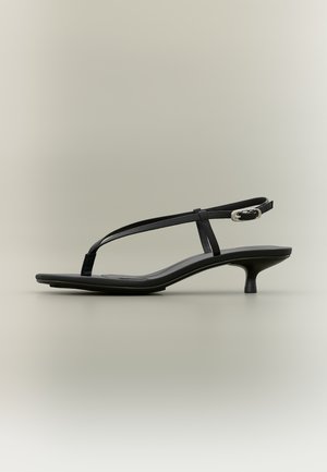 Zwarte sandaal met lage hak, dunne bandjes en een zilveren gesp, op een neutrale achtergrond.