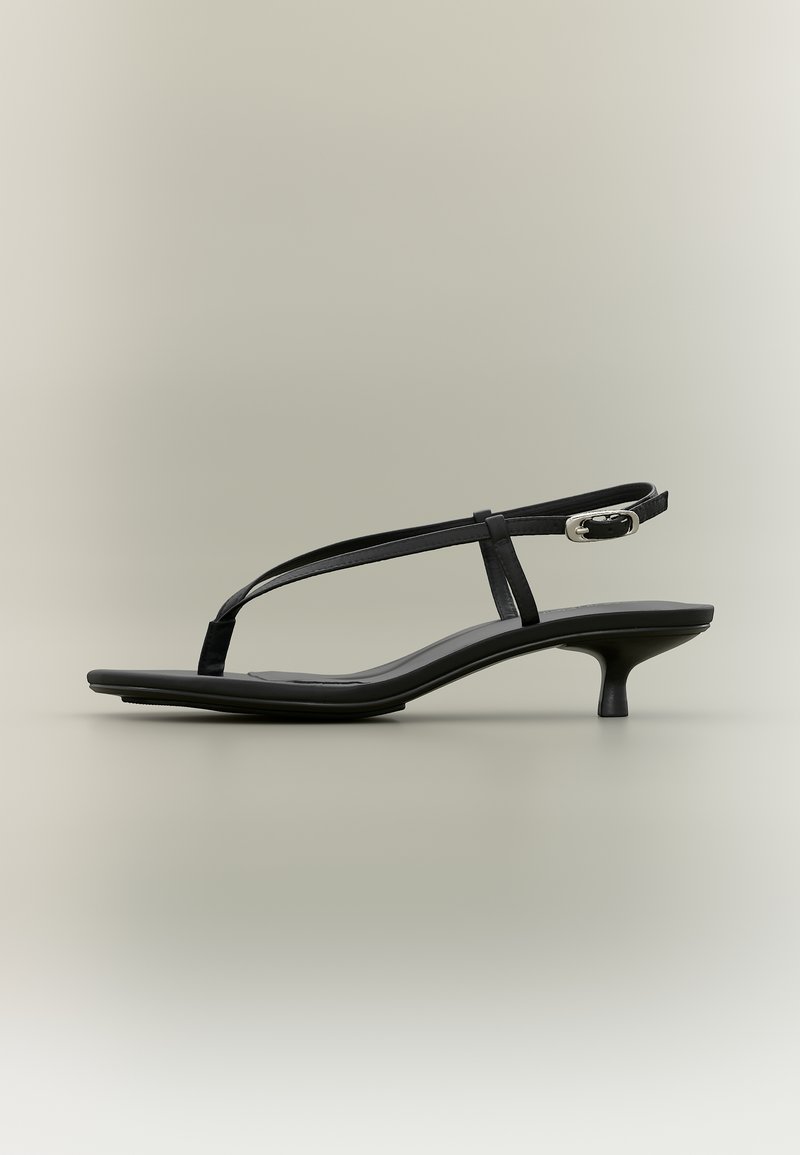 Črna nizko petna sandaleta s tankimi trakovi in srebrnim sponkom na nevtralnem ozadju.