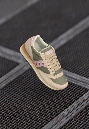Lichte sneaker in olijfgroen en beige leer, met een roze accent op de hiel, ronde neus en klassieke vetersluiting. Gelaagde zool.