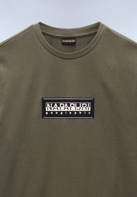 Oliven grøn t-shirt med rund hals, prydet med et sort rektangulært logo og hvid tekst "NAPAPIJRI geographic" i midten.