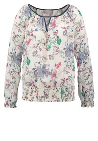 Blomstrig blus med en ljus krämfärgad bakgrund, prydd med flerfärgade blommönster, samlad halsringning och smockad nederkant. Långa ärmar.