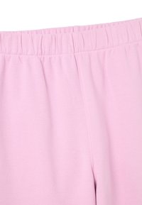 Pantalones de chándal rosa claro con cintura elástica y textura suave y lisa, con sutiles detalles de costura. Sin bolsillos visibles.