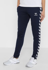 Marinefarbene Sporthosen aus dehnbarem Material, mit einem weißen Zickzackmuster an den Seiten und einem Logo auf der Vorderseite.