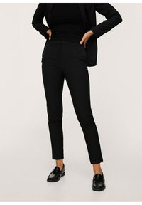 Pantalon noir sur mesure à coupe ajustée, avec une texture lisse et des poches avant. Associé à des mocassins noirs et un haut noir ajusté.