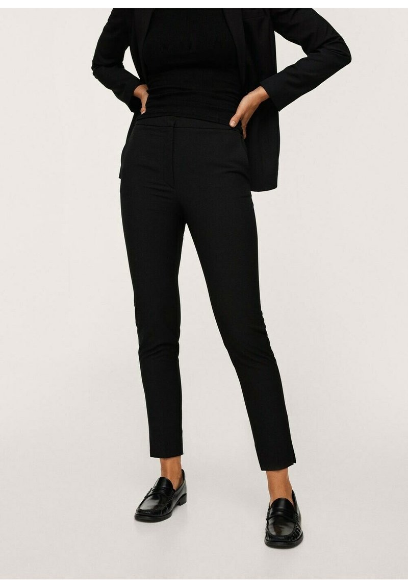 Pantalon noir sur mesure à coupe ajustée, avec une texture lisse et des poches avant. Associé à des mocassins noirs et un haut noir ajusté.