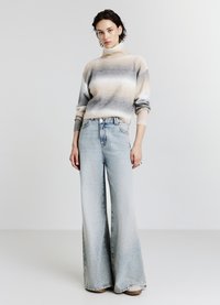 Maglione a collo alto a righe beige e grigie con maniche rilassate abbinato a jeans leggeri azzurri a vita alta e gamba larga. Texture morbide, vestibilità casual.