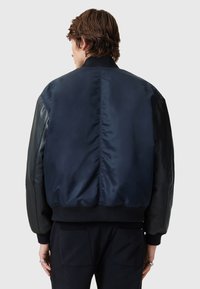 Navy bomber jacket with a glossy satin back and matte leather sleeves. Ribbed cuffs and waistband, featuring two side pockets.