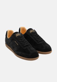 Schwarze Wildledersneaker mit einer Sohle aus Gummi, ausgestattet mit schwarzen Schnürsenkeln und einem hellbraunen Innenfutter. Das Logo "HENRY STEVENS" ist auf der Zunge eingestanzt.