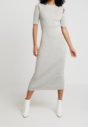 Grijze ribgebreide jurk met korte mouwen en open schouderdetails, met een halflange silhouet en gecombineerd met witte enkellaarzen.