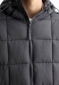 Schwarze Steppweste mit Steppmuster, Frontreißverschluss und verstellbarer Kapuze. Hergestellt aus glattem, leichtem Stoff mit mattem Finish.