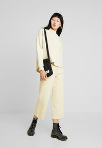 Világos sárga, túlméretezett pulóver, hozzá illő világos sárga, cropped nadrág és fekete fűzős csizma. Fekete, logós részletekkel ellátott keresztpántos táska.