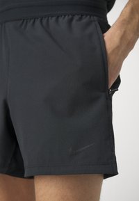 Mustad must sportlikud lühikesed püksid, millel on tekstuuriga kangas, elastne vöökoht, küljetaskud ja väike Nike logo alläärde lähedal.