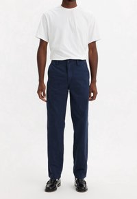Pantalon en coton bleu marine à coupe droite, associé à un t-shirt blanc uni à col rond, et des chaussures en cuir noires.