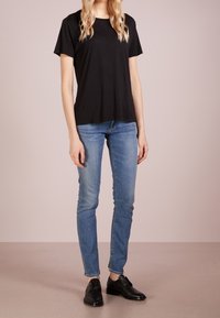 Svart kortärmad T-shirt med rund halsringning, kombinerad med ljusblå smal passform jeans och svarta skor. Slät tygtextur.