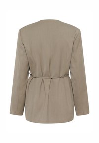 Gaiši brūns žakete ar garām piedurknēm, izceltu vidukli, pamatīgām krokojuma detaļām mugurpusē un gludu tekstūru, ar minimālisma dizainu.