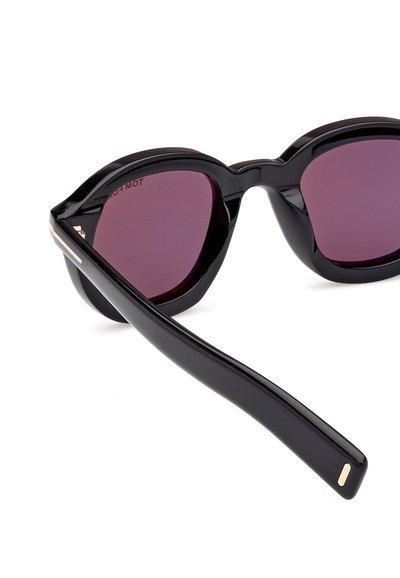 Lunettes de soleil noires en forme d'œil de chat, finition brillante et verres teintés en violet. Présentent une fine branche noire avec une accent en métal.