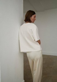 Top crem cu mânecă scurtă, cu croială lărguță, asortat cu pantaloni de culoare deschisă, cu croială slim-fit. Textură netedă, design minimalist, simplu, fără modele.