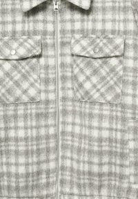 Šedá kostkovaná zipová bunda vyrobená z měkké, texturované látky, s dvěma náprsními kapsami na zpevněné zapínání a límečkovým výstřihem.