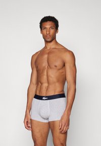 Boxers ajustados de algodón gris con una cinturilla elástica azul marino que presenta un logo blanco. El diseño tiene una forma ajustada y es suave al tacto.