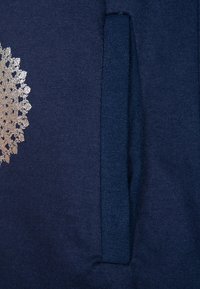 Granatowy materiał z pionową kieszenią i częściowym srebrnym wzorem kwiatowym po lewej stronie.