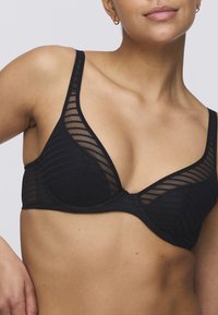 Musta verkkoliivit, joissa on kolmiomaiset kupit ja vaakasuora raidallinen kuvio. Säädettävät olkaimet ja tukevat kaaritukihaittavat ulkoasua.