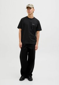 Schwarzes Baumwoll-T-Shirt mit kurzen Ärmeln und rundem Ausschnitt, kombiniert mit lockeren schwarzen Hosen und schwarzen Schuhen sowie einer beigen Kappe.