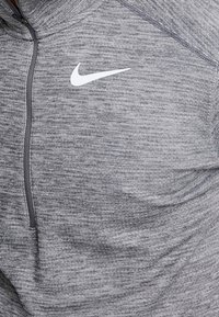 Maglia sportiva grigia a metà zip realizzata in tessuto testurizzato, con il logo Nike bianco nella zona sinistra del petto e una cerniera a contrasto.