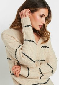 Maglione beige lavorato a maglia con righe nere, design a V, e polsini a coste. Texture morbida e vestibilità comoda. Ideale per un look casual.