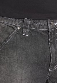 Svarta denimjeans med vit sydd detalj, som har en traditionell midja, knappstängning och en standard femfickorsdesign.