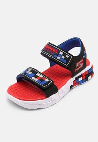 Mustat ja punaiset sandaalit siniset vivahteet, kuvioidut hihnat ja teksturoitu punainen pohja. Varustettu säädettävillä hihnoilla ja valkoisella pohjalla.