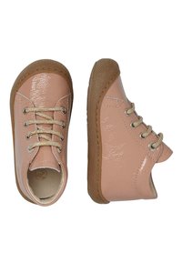 Zapatos de piel sintética de color rosa claro con acabado brillante, cordones crema y suela de goma marrón; diseño redondeado y detalle de talón descubierto.