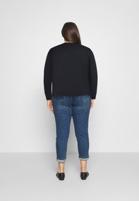 Zwarte sweatshirt met een relaxte fit en ronde halslijn, gecombineerd met lichtblauwe jeans met opgerolde mouwen. Zwarte instappers maken de outfit compleet.