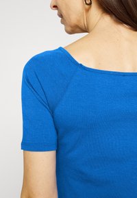 T-shirt blu a maniche corte con scollatura ampia, realizzato in morbido cotone, presenta maniche raglan e una texture liscia.