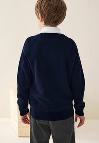 Pull en maille bleu marine avec des poignets et un ourlet côtelés, doté d'un col rond et de manches raglan, porté par-dessus un pantalon gris, vu de dos.
