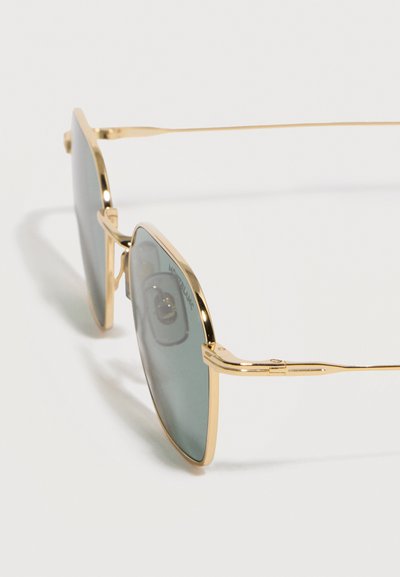 Γυαλιά ηλίου aviator με χρυσή μεταλλική κορνίζα, φακούς με σκούρο χρώμα και ρυθμιζόμενα μαξιλαράκια μύτης, σε απλό λευκό φόντο.