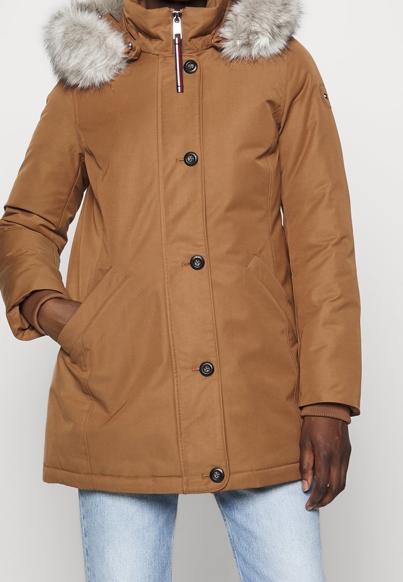 Parka imbottito marrone con cappuccio foderato di pelliccia, bottoni frontali, tasche laterali e polsini a coste. Tessuto liscio con finitura opaca.